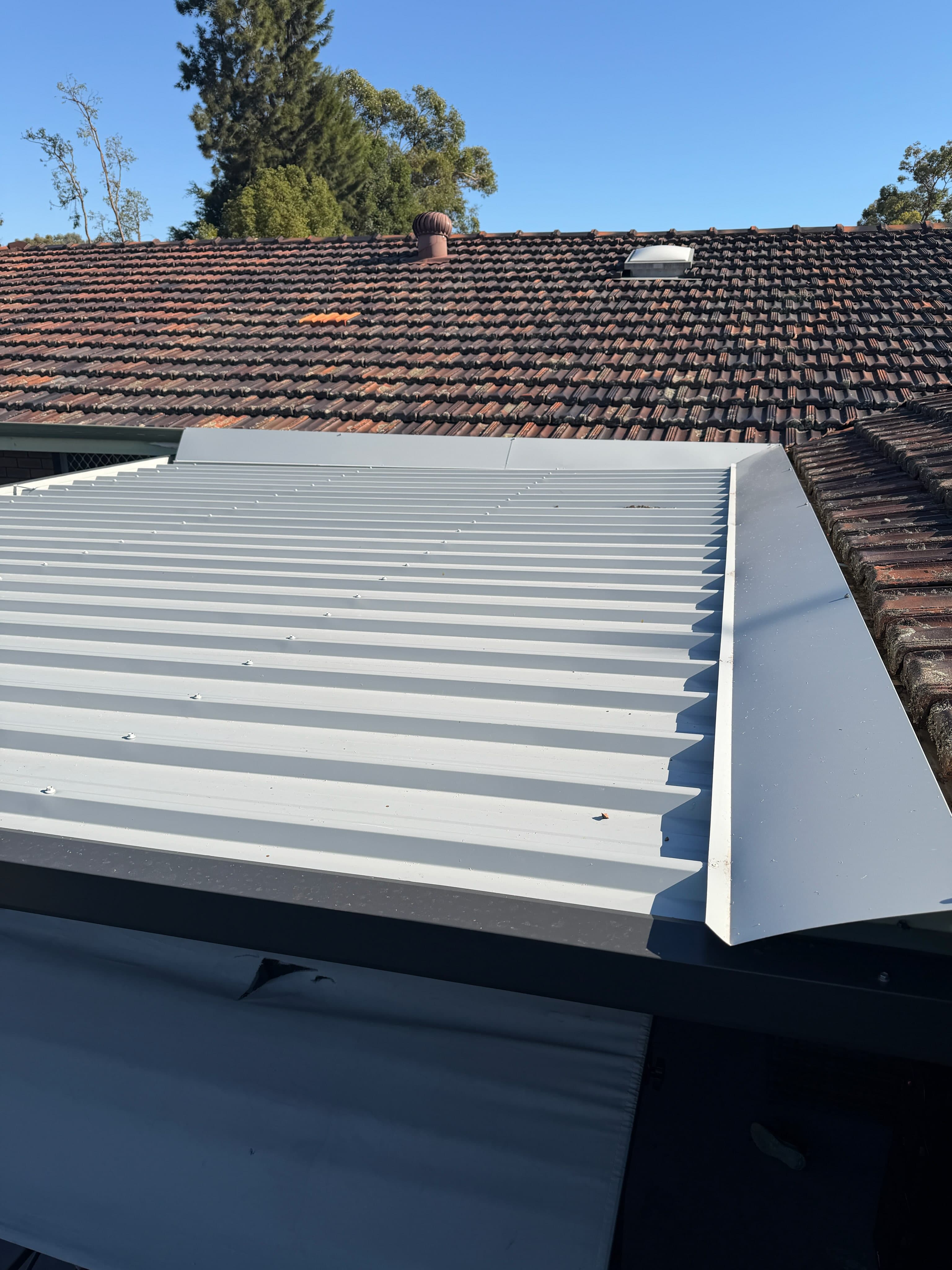 New Colorbond metal roof installed alongside existing terracotta tile, with crisp flashings